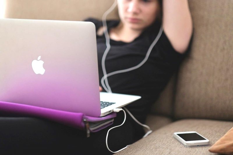 アップル社のノートパソコンを使って音楽を聴く若い女性。