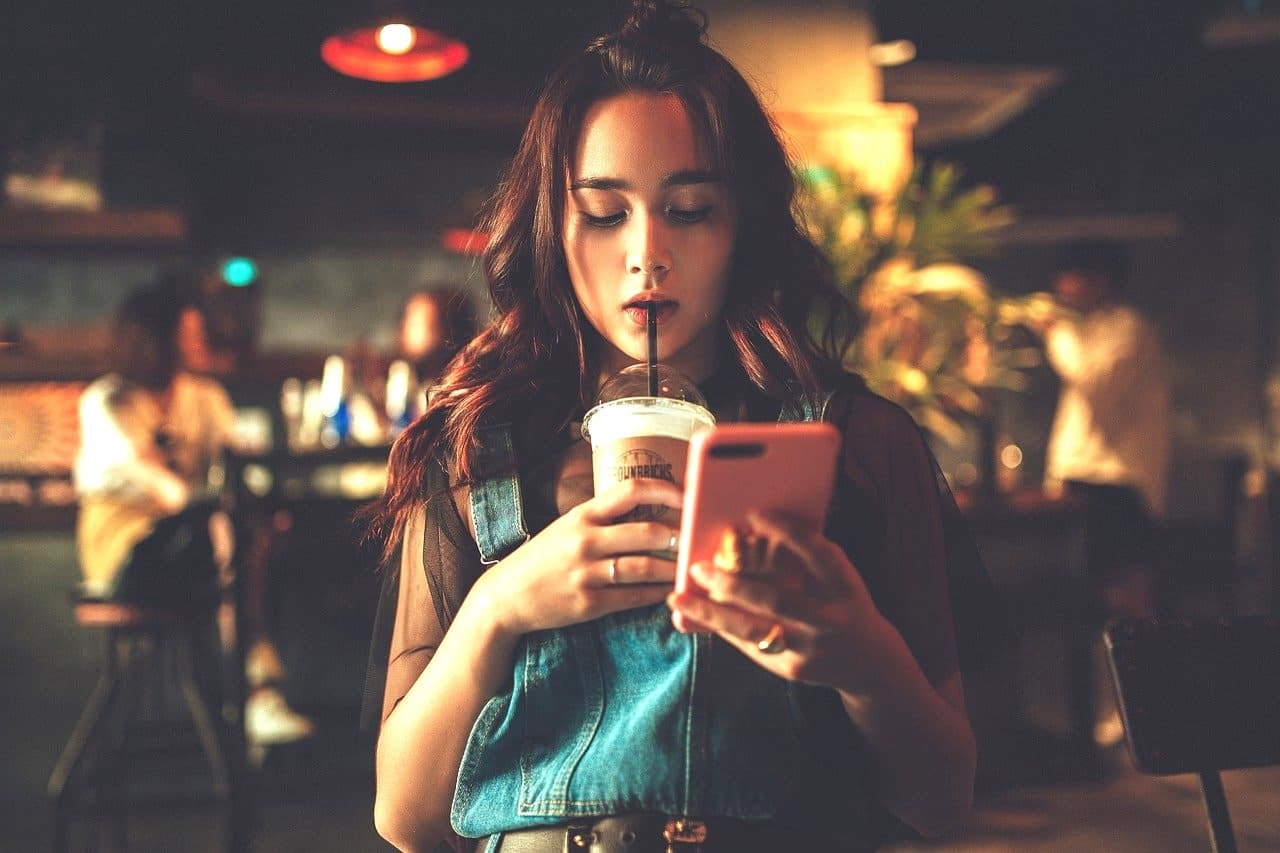スマートフォンを操作しながらジュースを飲む美少女。