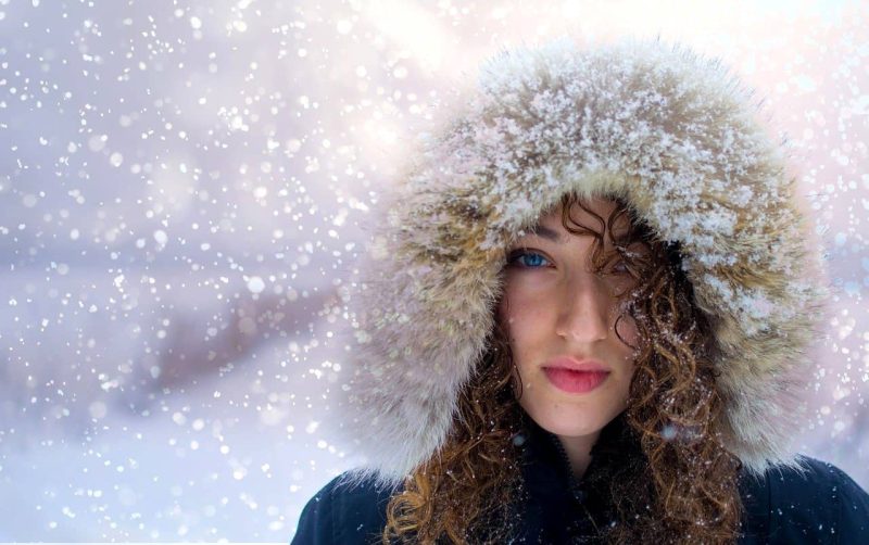 雪が降る中、フードをかぶっている若い女性。